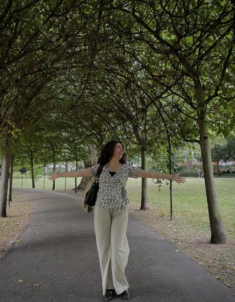 Mariam Al-Khadhar med udstrakte arme, der står under en bue af træer på en sti i en park